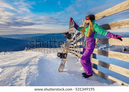 Successful young girl snowboarding in the mountains Sheregesh. Snowboarder resting.  Stylish caucasian snowboarder. Snowboarder  on top of the mountain on a background of blue sky. 