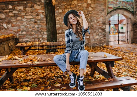 Jeune femme sans souci dans un pantalon vintage branché assise sur une table dans le parc et riant. Jeune fille mignonne et curieuse de bonne humeur posant en automne, profitant du beau temps.