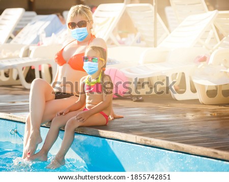 Young toddler girl playing in a water paddling pool wearing a face mask due to Coronavirus outbreak