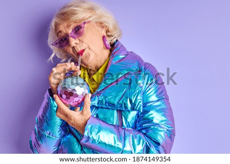 senior lady in bright coloured clothes posing at camera, drinking juice or other beverage, at party