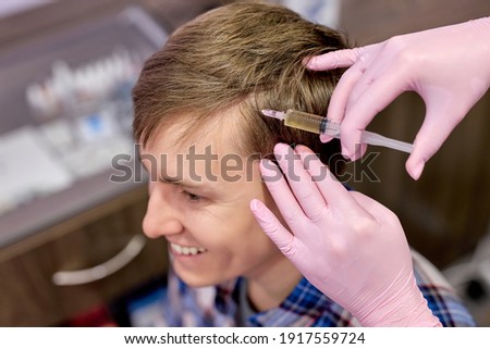 male person at trichologist office get injections in head skin. cropped doctor hands holding syringe under patient's head. procedure against hair loss and for skin health. beauty and medicine concept