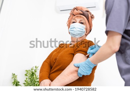 cheerful young nurse giving a vaccine injection to elderly woman at home