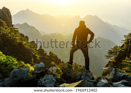 Young man standing in the summer mountains at sunrise and enjoying view of nature.