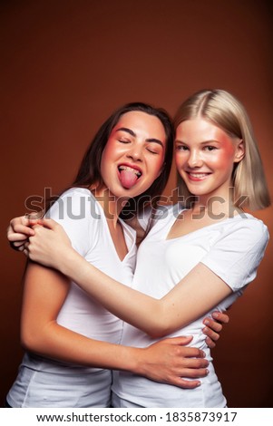 wo pretty diverse girls happy posing together: blond and brunette on brown background, lifestyle people concept