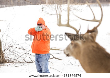 Deer hunter in orange taking aim at a whitetail deer. Focus on hunter