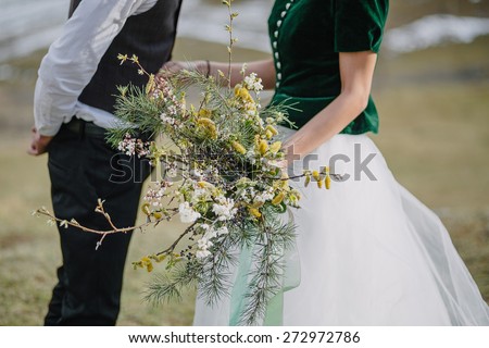 couple holding wedding bouquet of pine branches and greenery in rustic style on a background of snowy mountains