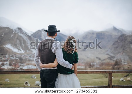 couple standing on the platform with a wooden handrail with beautiful views of the mountains and the snow-capped peaks