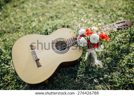 wedding bouquet of red and white flowers and greenery near a guitar on the green grass