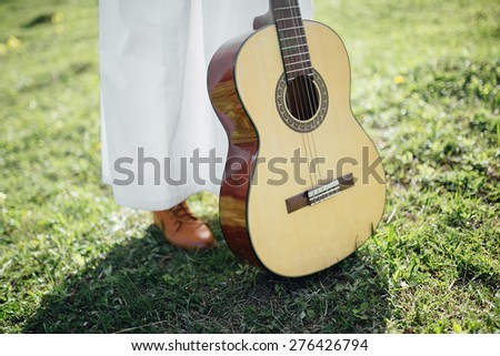 bride in a white vintage dress and brown leather boots with a guitar standing on the green grass