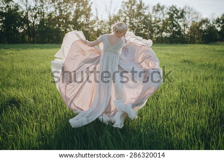 bride wedding dress develops in the air against green field and sunset
