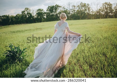 woman in a wedding dress walking along a green field on the background of the forest at sunset, the bride and groom