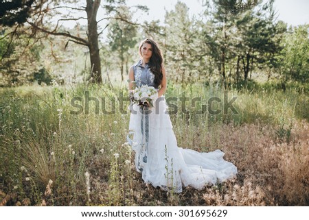woman in a wedding dress with a bouquet of white flowers and greenery is a clearing in the pine forest
