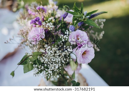 decoration of flowers and greenery on the holiday table, which stands on a green lawn in a pine forest