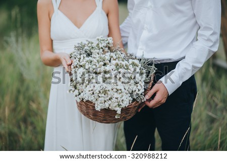 the guy in the white shirt and the girl in white dress holding a basket with white flowers on a background of green hills