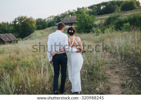the guy in the white shirt and the girl in white dress walk on the road against the backdrop of green hills
