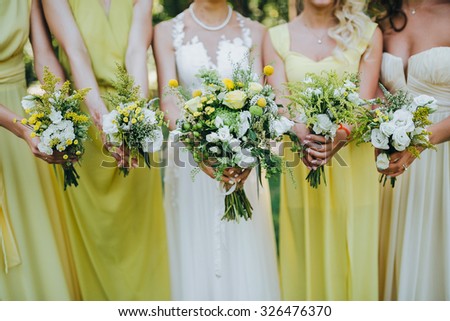 bride in a white dress and bridesmaids dresses are yellow and are holding bouquets of yellow flowers and greenery