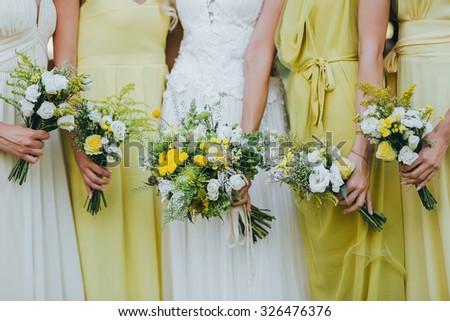 bride in a white dress and bridesmaids dresses are yellow and are holding bouquets of yellow flowers and greenery