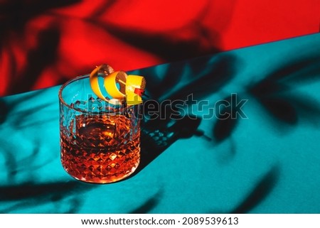 Sazerac, classic alcoholic cocktail with cognac, bourbon, absinthe, bitters, sugar and lemon zest. Dazzling red blue background with hard light and harsh shadows Photo stock © 