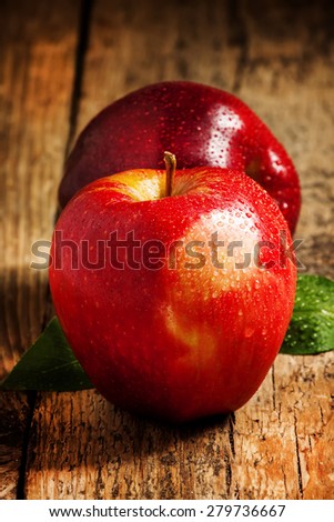 Two red apples with water drops on a wooden table, selective focus