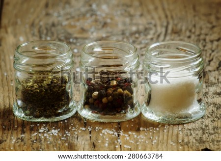 Spices: salt, pepper and herbs in small glass jar on a wooden table, selective focus
