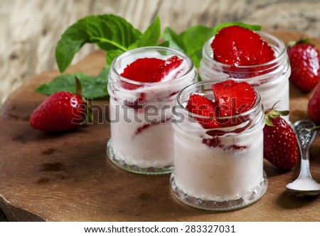 Homemade strawberry yogurt with fresh wild strawberries and mint in a jar on a wooden board, selective focus