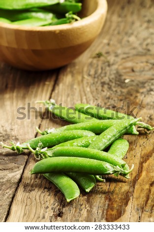 Pods of fresh green peas in a bowl on old wooden table, selective focus