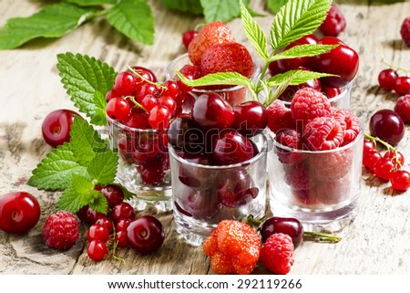 Assorted summer berries: raspberries, red currant, cherry, strawberry with glasses on an old wooden table, selective focus