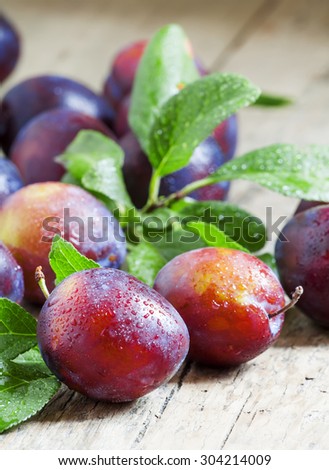 Delicious blue-orange plums with drops of water on the old wooden background, selective focus