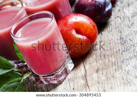 Delicious fresh juice of red and blue sweet plums and peach in a glass on the old wooden background, selective focus