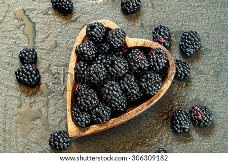 Fresh blackberries in a bowl in the shape of a heart on a dark background, top view, toned image, selective focus