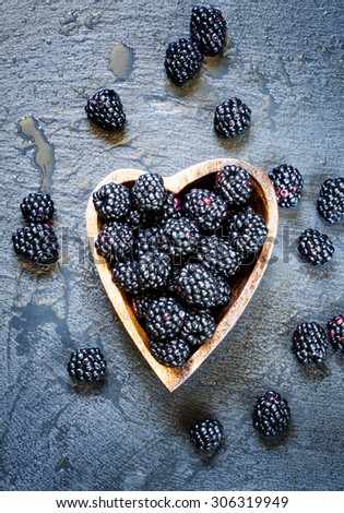 Fresh blackberries in a bowl in the shape of a heart on a dark background, top view, toned image, selective focus