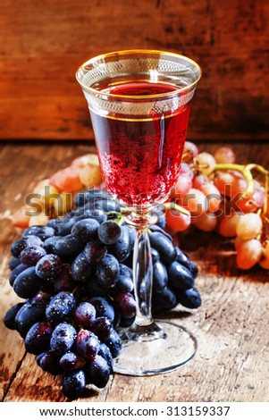 Red sparkling wine in the glass, blue and pink grapes in the wine cellar, selective focus
