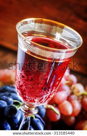 Red sparkling wine in the glass, blue and pink grapes in the wine cellar, selective focus