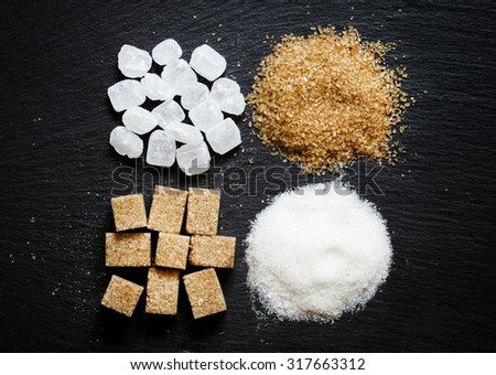 Assortment of sugar: white sand, candy sugar, brown sugar into pieces and brown sugar on a dark background, top view