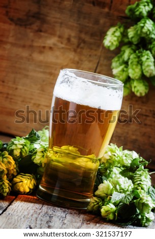 glass of foamy beer and hop cones on old wooden background, selective focus