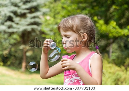 little girl in the park inflates soap bubbles in the park