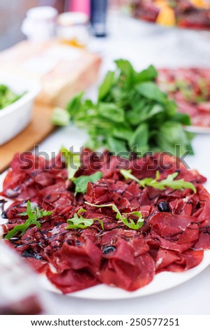 Smoked and sliced meat on dish near green leafs