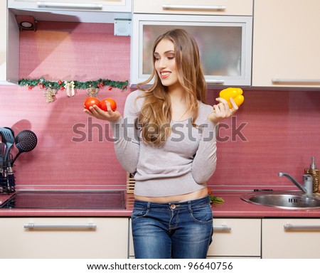 Attractive young woman with tomato and pepper smiling and joyful looking out of the camera in the modern kitchen