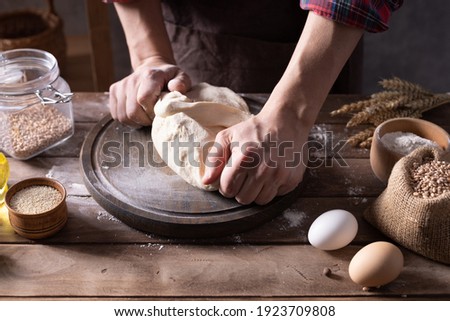 Baker man kneading or making dough and bakery ingredients for homemade bread cooking on table. Bakery concept with male hand and dough wooden tabletop background texture