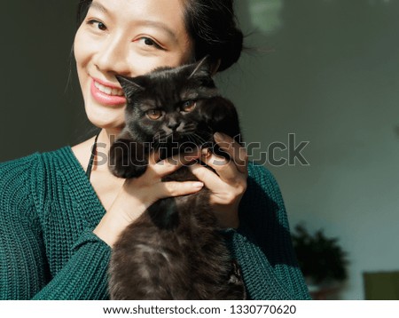 Portrait of beautiful Chinese young girl hug her cute British Shorthair Cat who has amazing orange eyes at home and smile at camera in sunny afternoon, happy pets owner lifestyle.