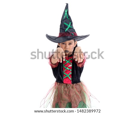 Asian little girl in costume of witch is stretching hand forward. Cute child shows face and gestures to trick others into fear. Childhood fun with Halloween activities.