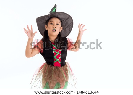 Asian little girl in costume of witch is stretching hand forward. Cute child shows face and gestures to trick others into fear. Childhood fun with Halloween activities.