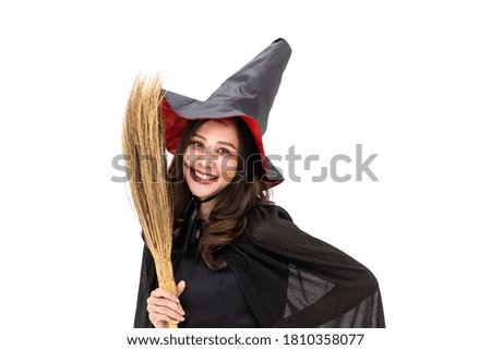 Asian woman wearing Halloween costume as witch in black cloak, on white background, holding broomstick, looking at camera