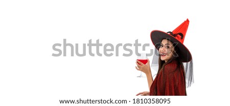 Asian woman wearing Halloween costume as witch in red cloak, on white background, holding red wine glass, looking at camera