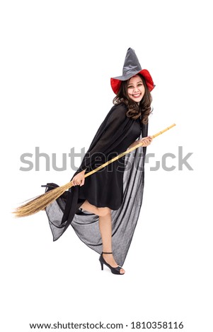 Asian woman wearing Halloween costume as witch in black cloak, on white background, holding broomstick, looking at camera