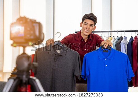 Young Asian male online merchant blogger using camera to live video to review and sell product. Social media, Influencer, and online shopping concept.