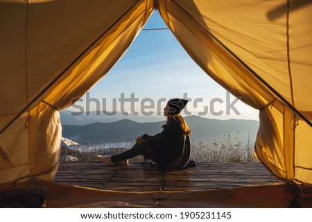 A female traveler sitting on wooden balcony while watching a beautiful mountains and nature view outside the tent