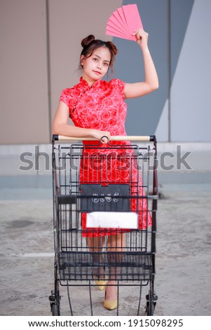 Big summer sale Chinese New Year Festival! Beautiful gorgeous Asian woman in traditional Chinese dress holding Ang Pow and pushing supermarket cart.
