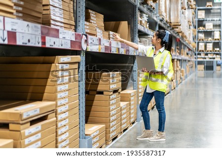 Asian engineer woman check stock details on tablet computer for checking boxes with logistics on shelves with goods background in warehouse, logistic and business export