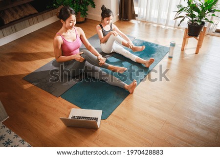 Asian woman and Little girl practicing yoga from yoga online course via laptop at home.